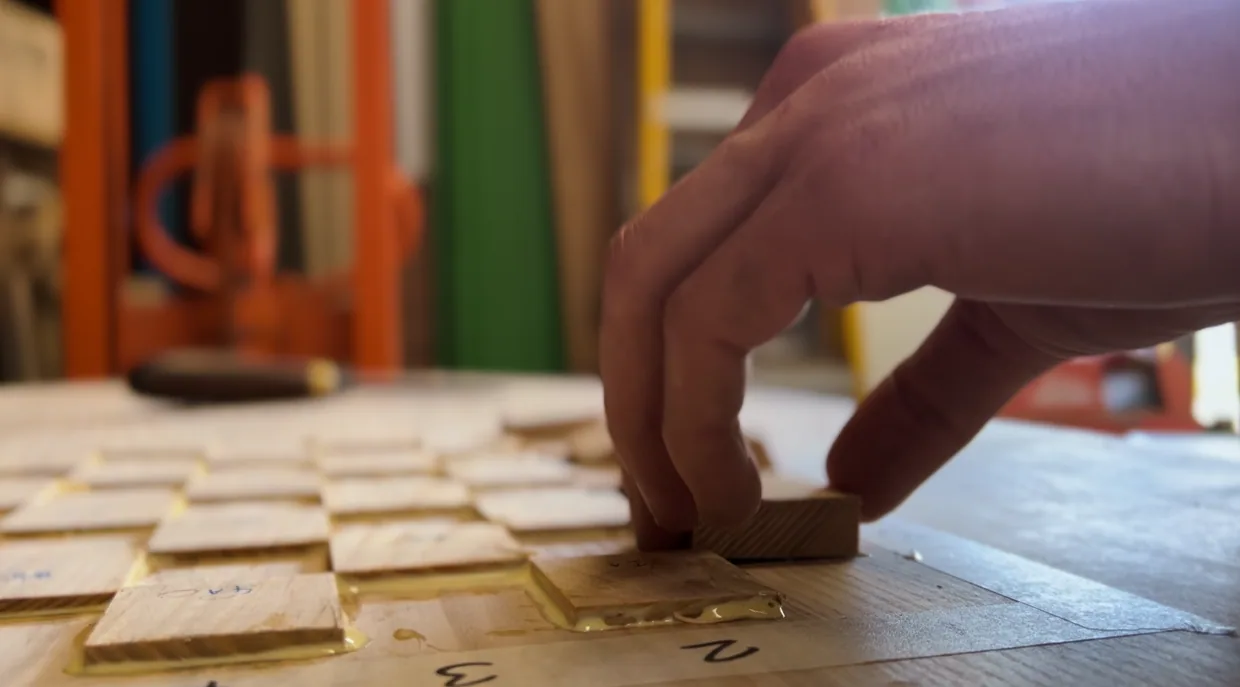 Hand laying light and dark timber squares for a chessboard on the workshop bench